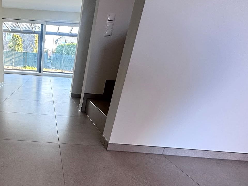 Flur mit großformatigen Bodenfliesen und Sockelleiste, im Hintergrund die Treppe und große Fenster
